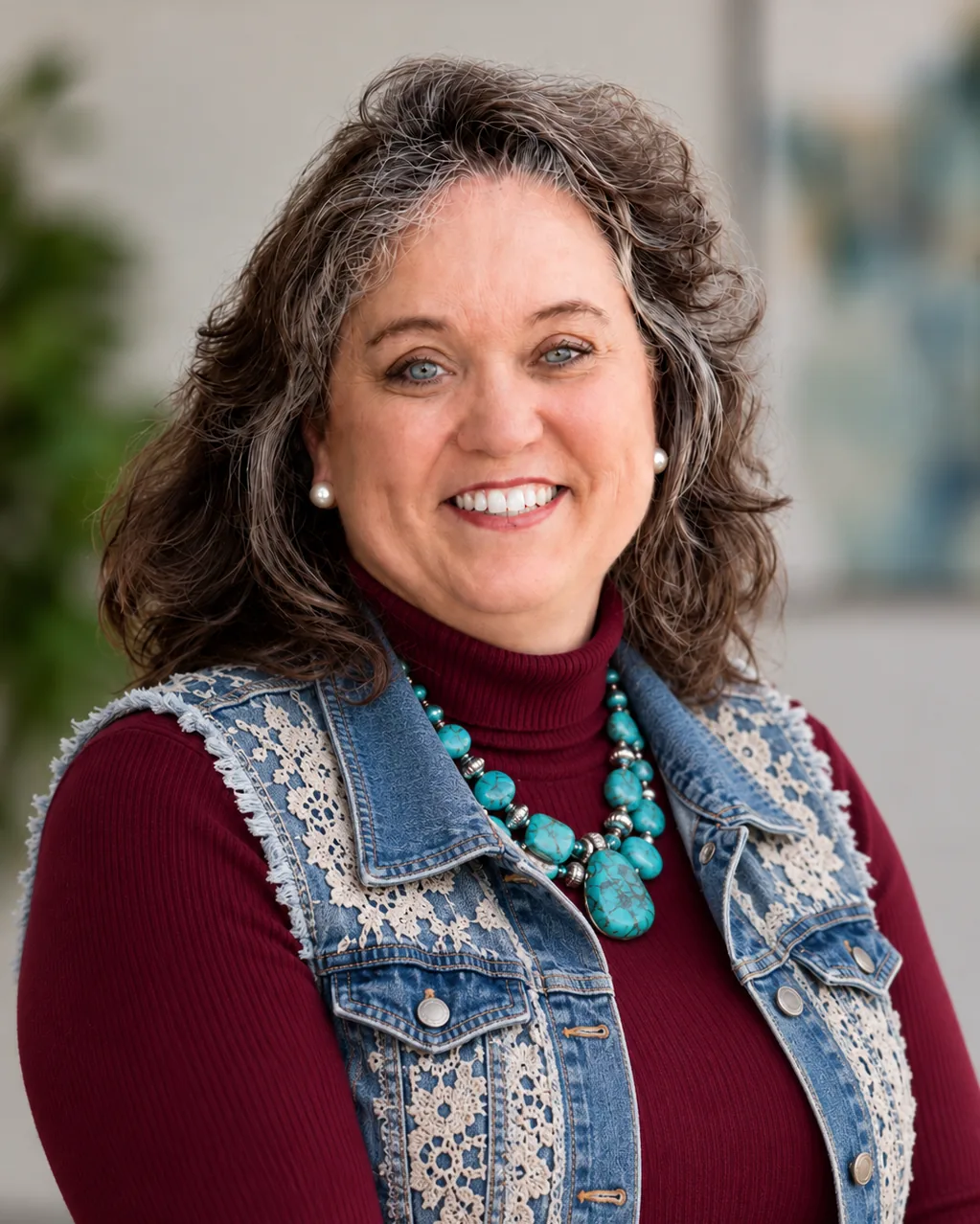 Becky Pool smiling, wearing a lace-trimmed denim vest over a maroon top with a turquoise necklace